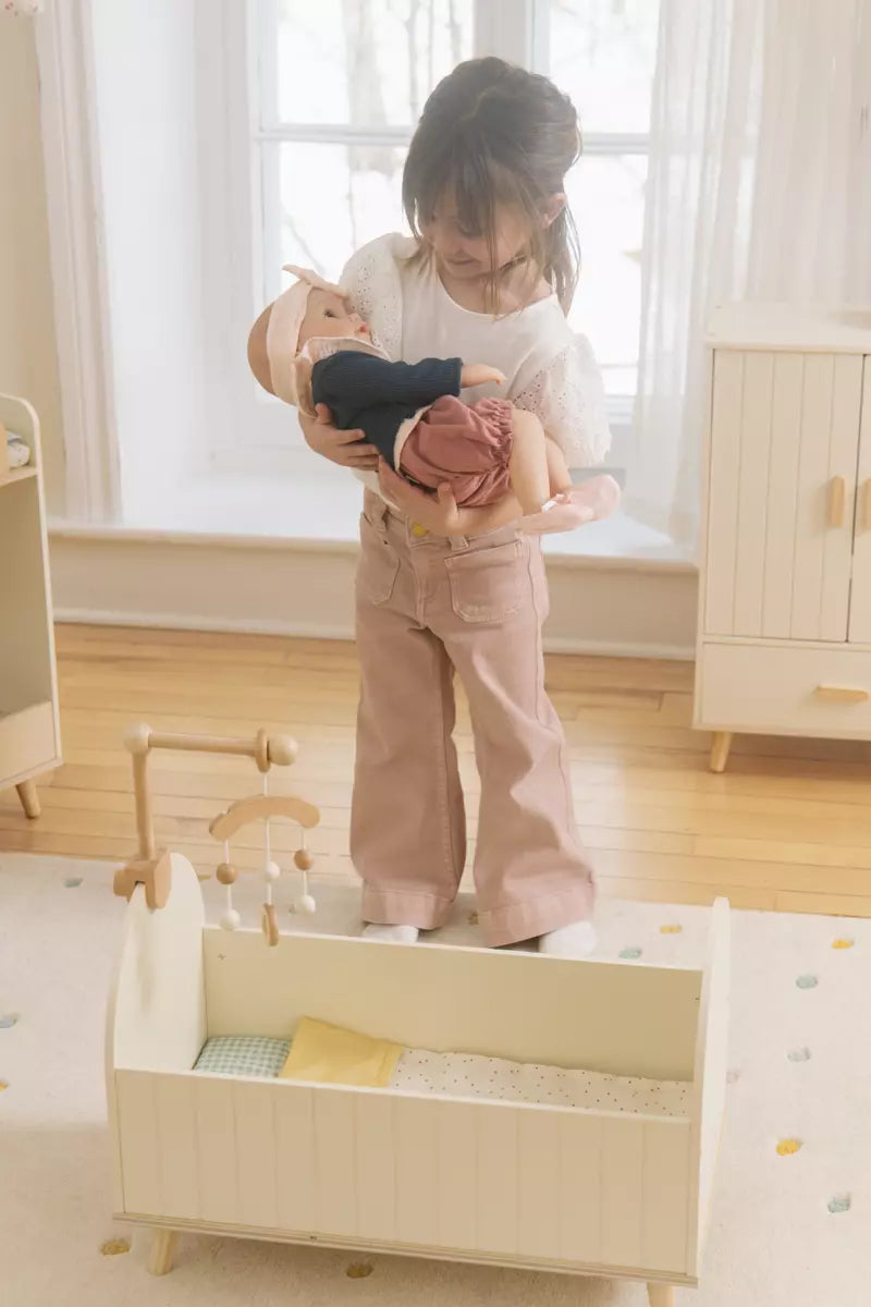 Person holding a baby doll in a nursery with a crib and dresser.