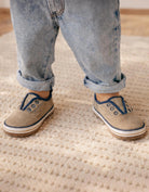 Person wearing beige shoes with blue laces and rolled-up jeans standing on a textured carpet.