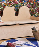 Wooden bench with storage compartment against a floral wall.