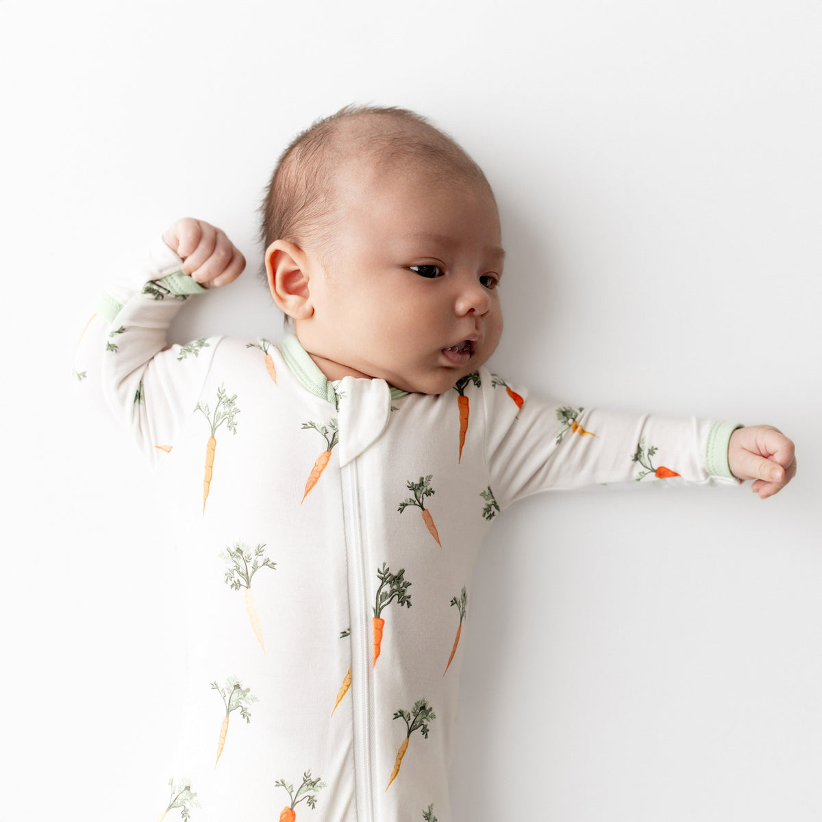 Baby wearing a onesie with carrot pattern on a white background