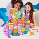 Two children playing with colorful magnetic building blocks on a white surface.