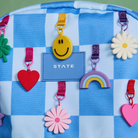 Colorful keychains and charms on a blue checkered background with 'STATE' branding.