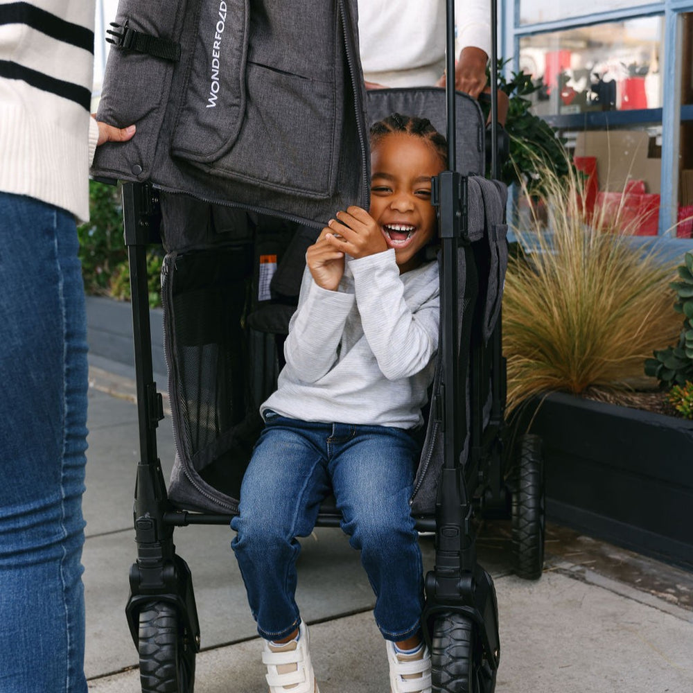 Child sitting in a stroller with a WonderFold logo, smiling outdoors.
