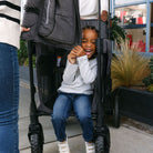 Child sitting in a stroller with a WonderFold logo, smiling outdoors.