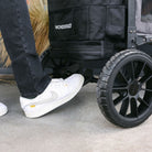 Person wearing white sneakers stepping onto a black WonderFold stroller.