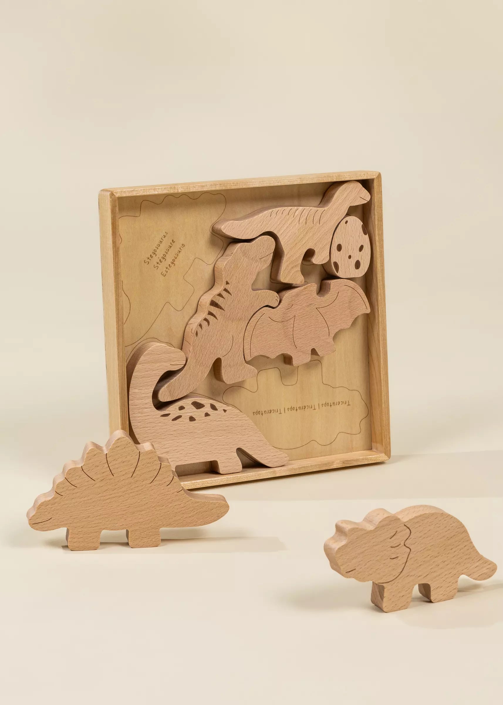 Set of wooden dinosaur toys with a box on a beige background
