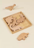 Set of wooden dinosaur toys with one toy outside the box on a beige background
