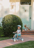 Child riding a tricycle in front of a house with a blue door.
