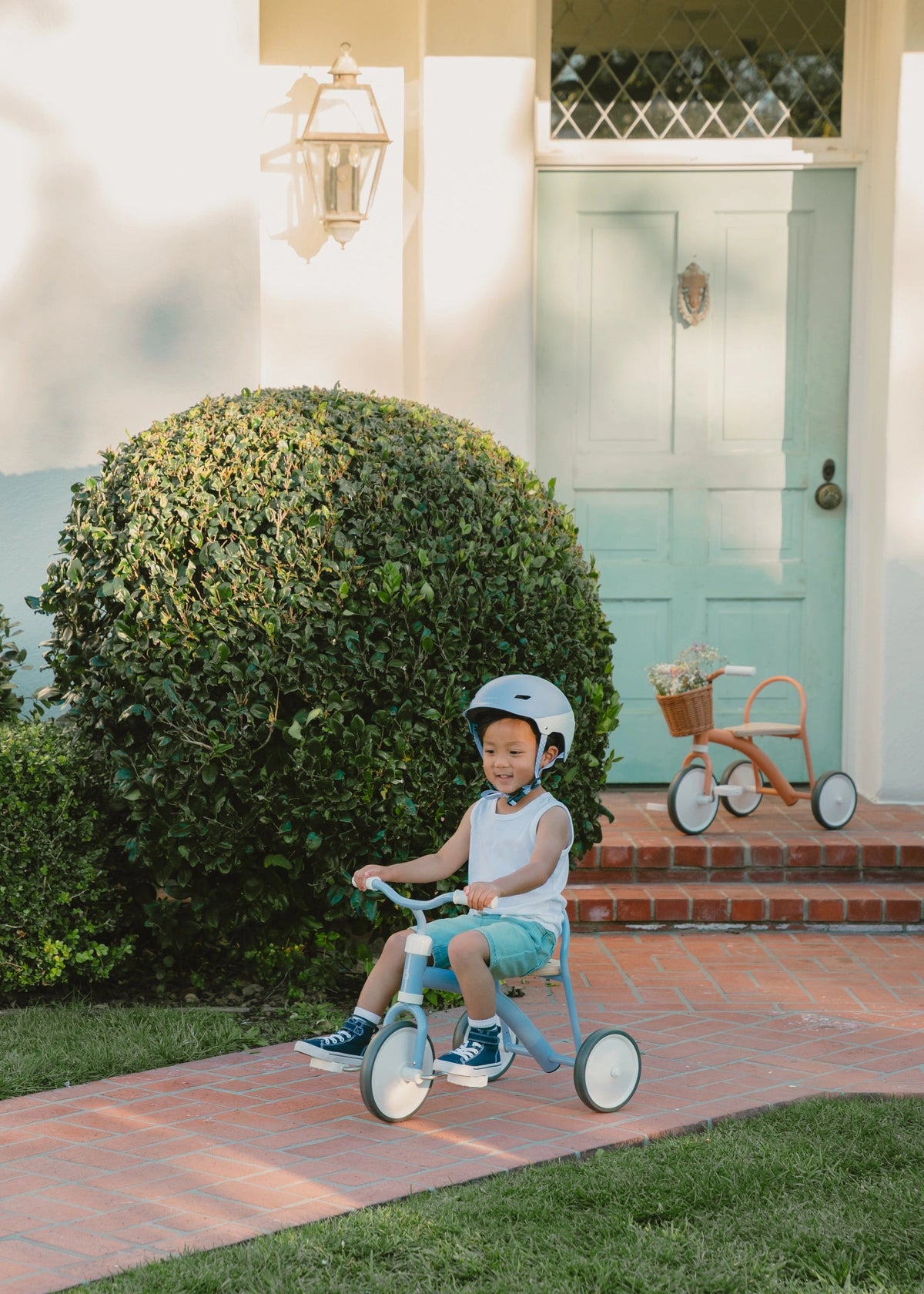 Child riding a tricycle in front of a house with a blue door.