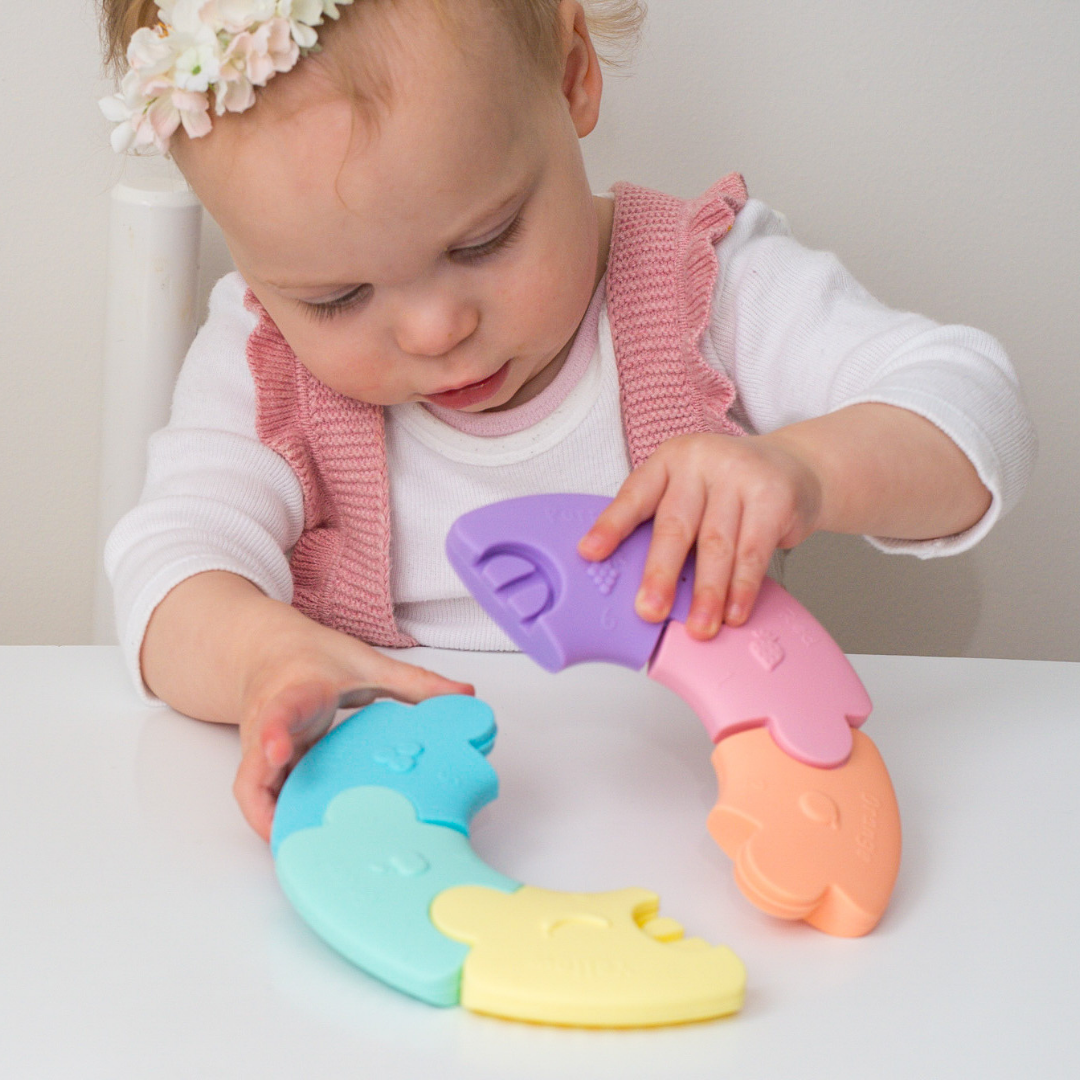 Child playing with colorful silicone teething rings on a white surface.