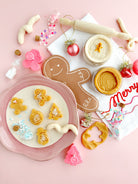 Decorative cookies shaped like gingerbread men and trees on a pink surface with cookie cutters and festive decorations.
