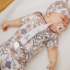 Baby sleeping in a floral outfit with a pacifier, on a soft surface.