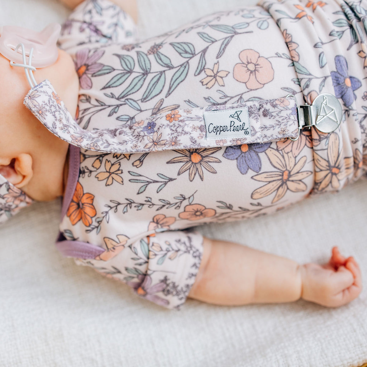 Baby in floral outfit with 'Copper Pearl' branding on a soft surface