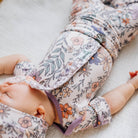 Baby wrapped in a floral swaddle with a visible brand label on a soft surface.
