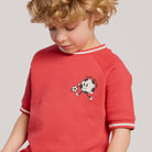 Child wearing a red shirt with a graphic design on a plain background