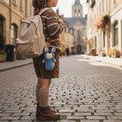 Person walking down a cobblestone street with a backpack and blue plush toy