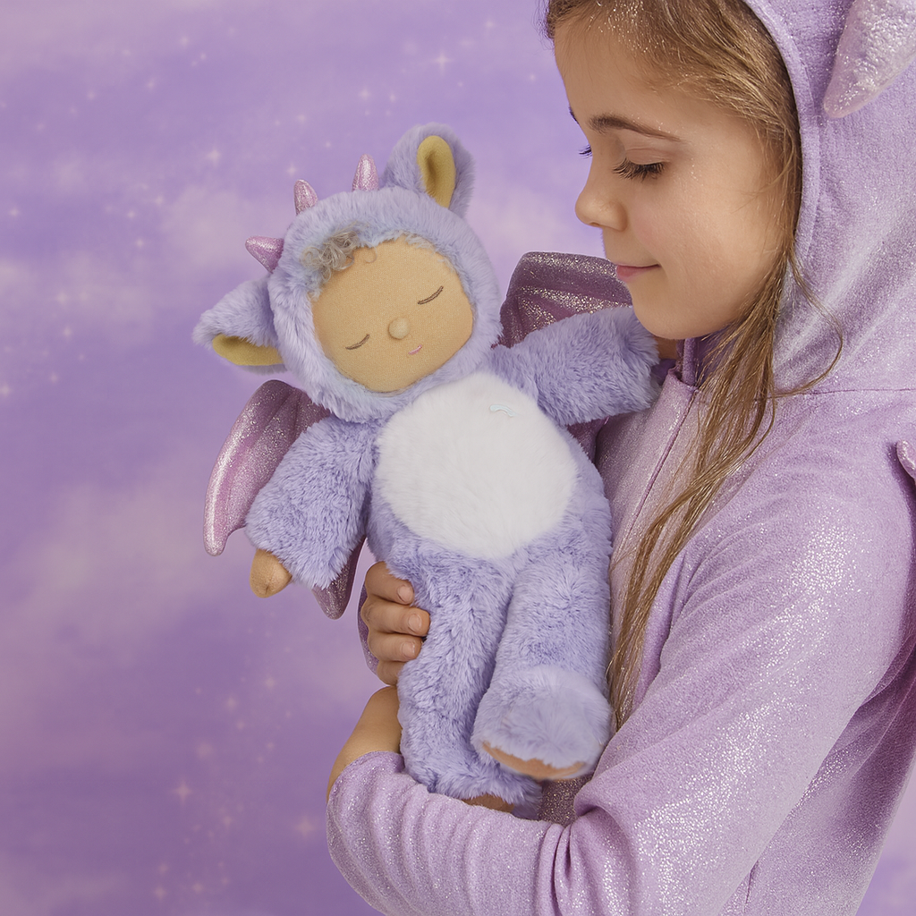 Child in a purple onesie holding a plush toy with a purple background