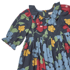 A close-up of a children's dress with a dark navy blue base and a colorful floral print featuring red, yellow, and light blue flowers with green leaves. The dress has a ruffled collar, long sleeves with elastic cuffs, and a gathered waist.