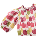 A baby smocked blouse with puff sleeves, featuring a colorful pattern of red, pink, yellow, and green apples on a white background.