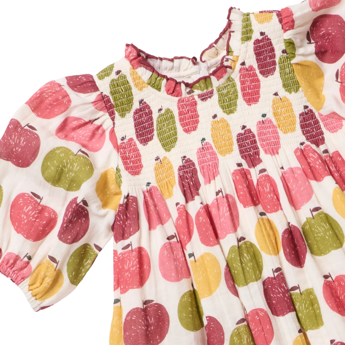 A close-up of a children's dress with a white base and an all-over apple print in pink, red, yellow, and green. The dress features a smocked bodice, ruffled neckline, and short puff sleeves.