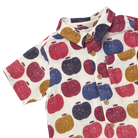 A short-sleeve button-up shirt with an all-over apple print on a cream background. The pattern features red, navy blue, and mustard yellow apples, with matching red and navy accents on the collar and a chest pocket.