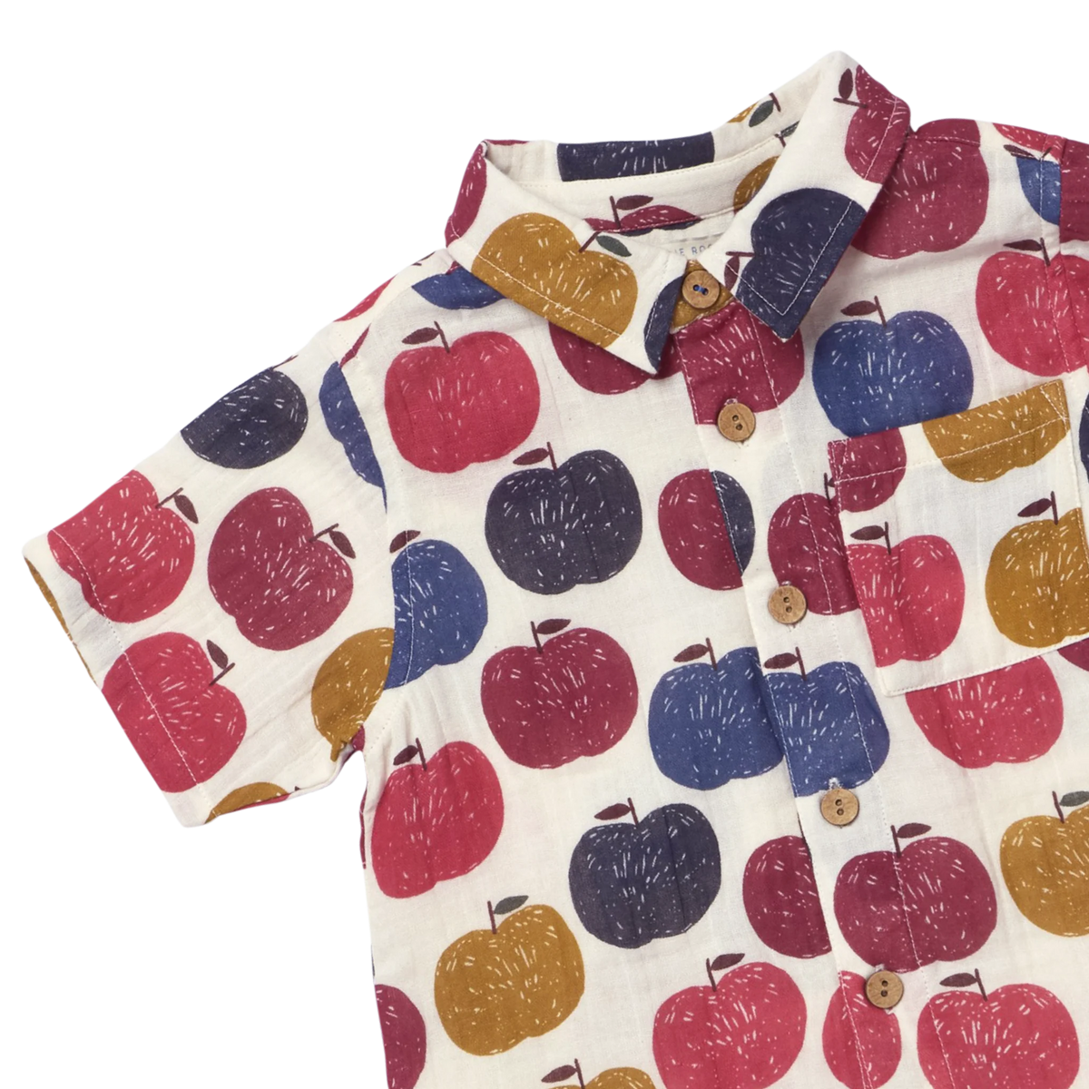 A short-sleeve button-up shirt with an all-over apple print on a cream background. The pattern features red, navy blue, and mustard yellow apples, with matching red and navy accents on the collar and a chest pocket.