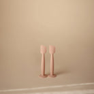 Two pale pink silicone spatulas standing upright on a matching round base against a warm beige background.