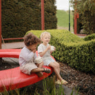 Two children sitting on a red bench in a garden setting.