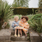Two young children sitting together outdoors on stone steps in a garden, playing with a wooden alphabet puzzle on a small low table.