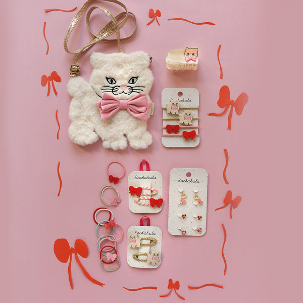 Collection of cat-themed hair accessories on a pink background with decorative bows.