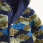 Close-up of a sherpa fleece zip-up jacket with a geometric wavy pattern in navy blue, olive green, light blue, and cream, featuring a solid navy hood.