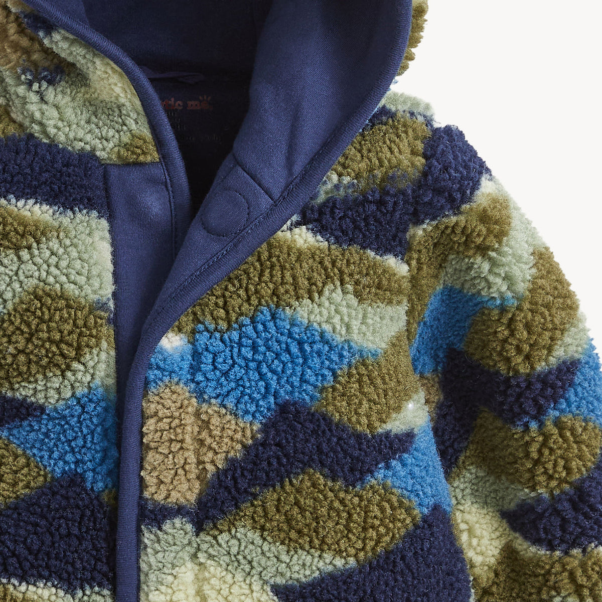 Close-up of a sherpa fleece zip-up jacket with a geometric wavy pattern in navy blue, olive green, light blue, and cream, featuring a solid navy hood.