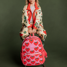 Person holding a pink backpack with red heart patterns against a green background