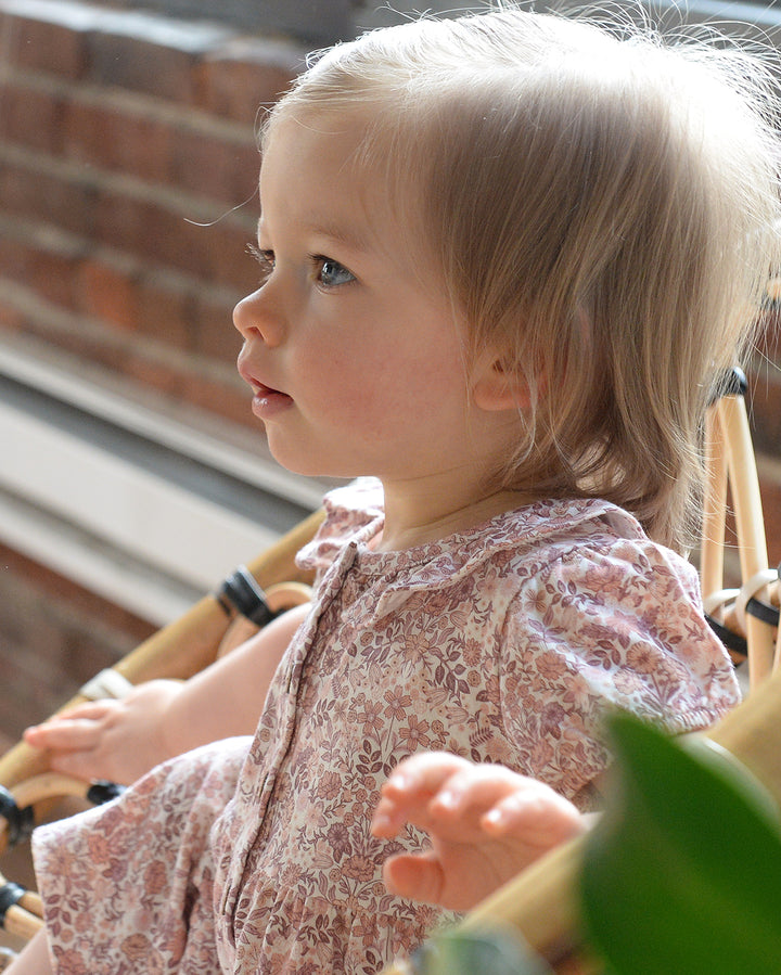 Young child in a floral dress sitting outdoors with a blurred background