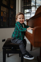 Child sitting on a piano bench in a room with large windows.