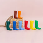 Colorful rubber boots arranged in a row with a straw bag on a light pink background
