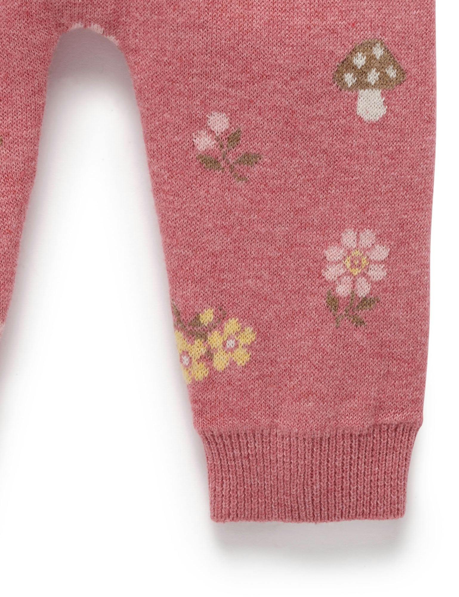 Close-up of a pink knit garment leg with a ribbed cuff, featuring small floral and mushroom motifs in white, yellow, green, and brown.