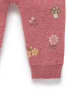 Close-up of a pink knit garment leg with a ribbed cuff, featuring small floral and mushroom motifs in white, yellow, green, and brown.