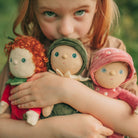 Child holding three dolls with different outfits against a blurred green background