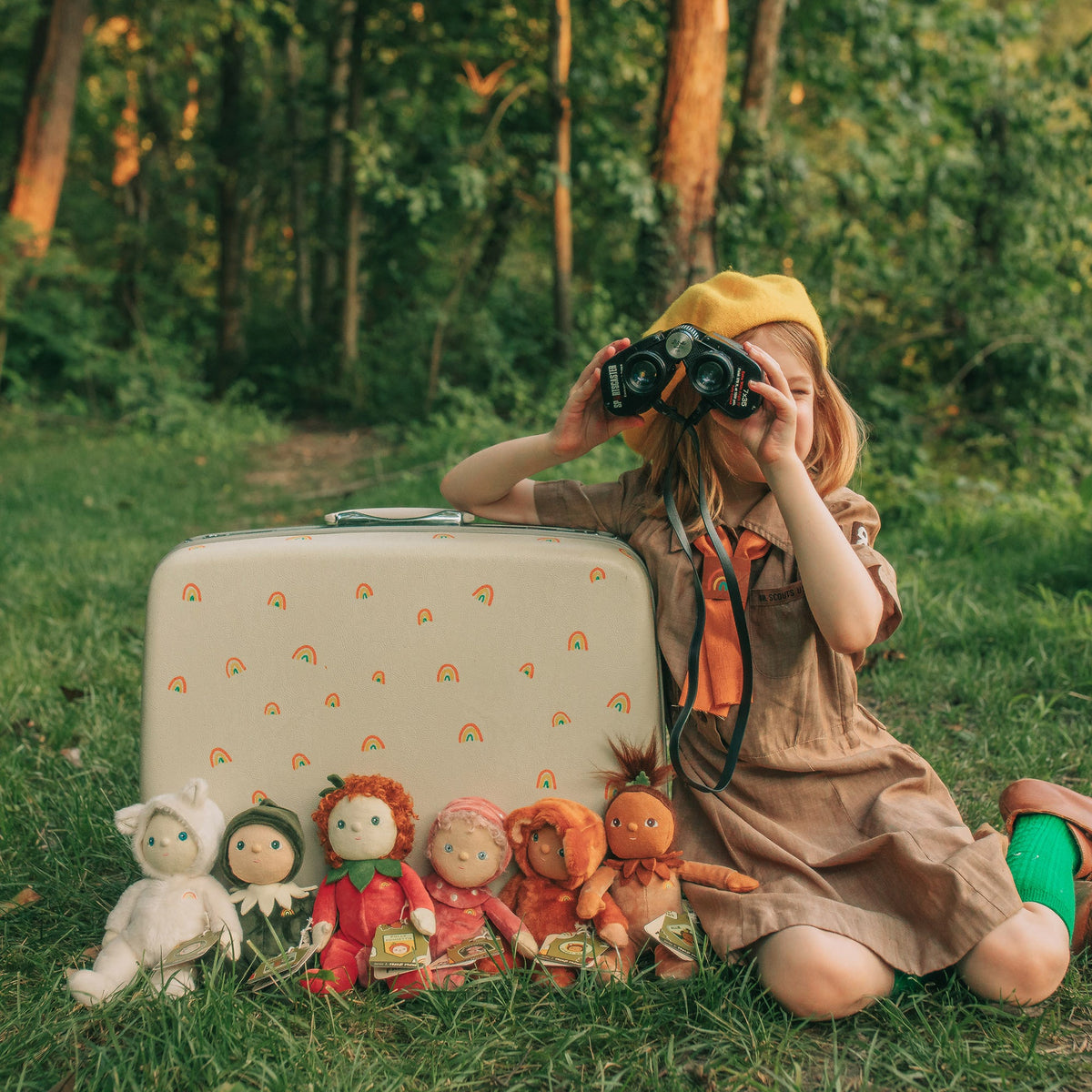 Child in a forest setting with a vintage suitcase, camera, and dolls.