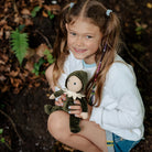 Young girl holding a doll in a forest setting