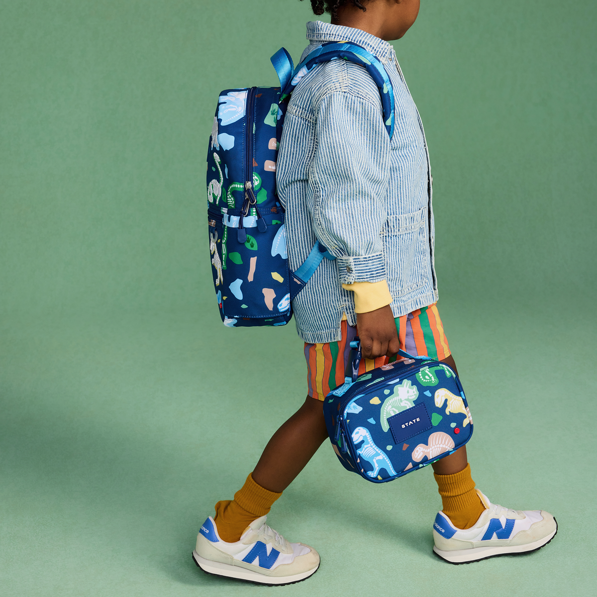 Child wearing a blue backpack with dinosaur pattern on a green background