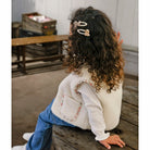 Child sitting on a wooden bench wearing a white jacket with floral details and blue jeans.