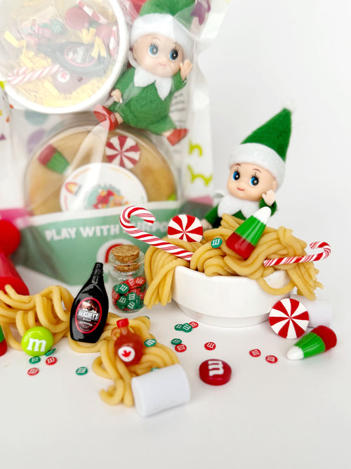 Elf figurines with candy canes and M&M's on a white surface