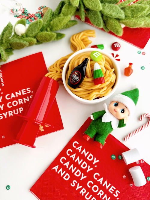 Christmas-themed setting with candy, elf figurine, and M&M's on a white surface.