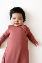 A baby lying on their back wearing a dusty rose long-sleeve swaddle blanket against a clean white background.