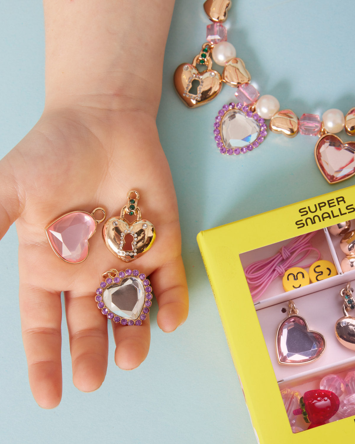Heart-shaped jewelry on a child's hand with a 'Super Smalls' box in the background