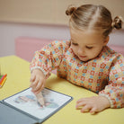 Child interacting with a tablet on a yellow table