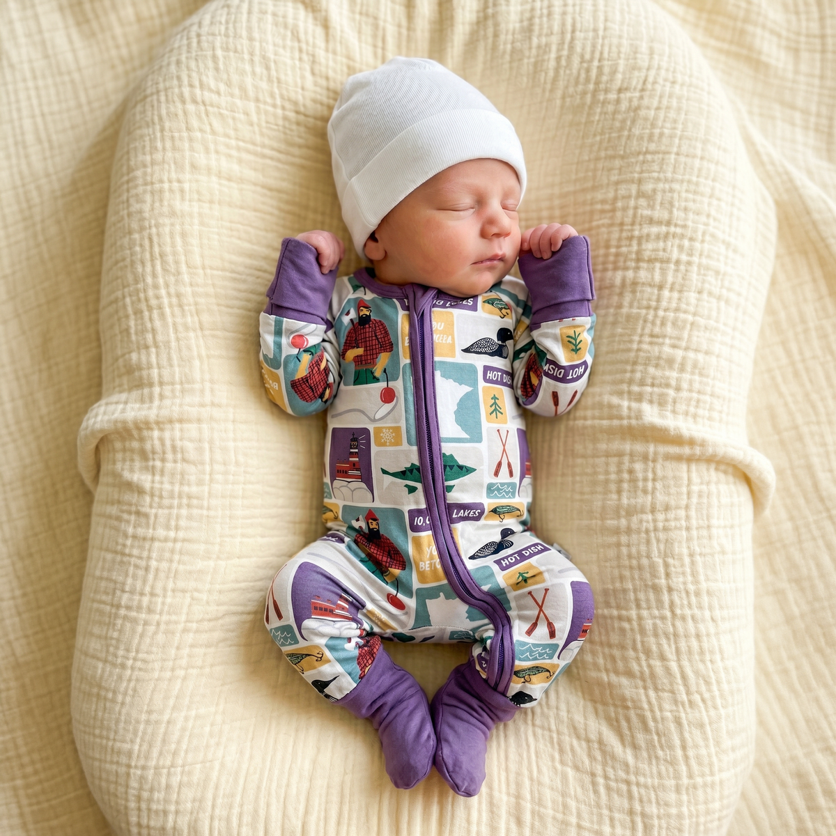 Newborn baby in a colorful outfit and white hat lying on a textured beige surface