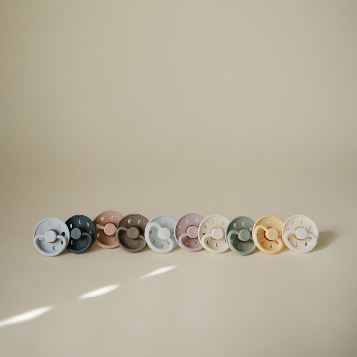 Row of colorful pacifiers on a beige background